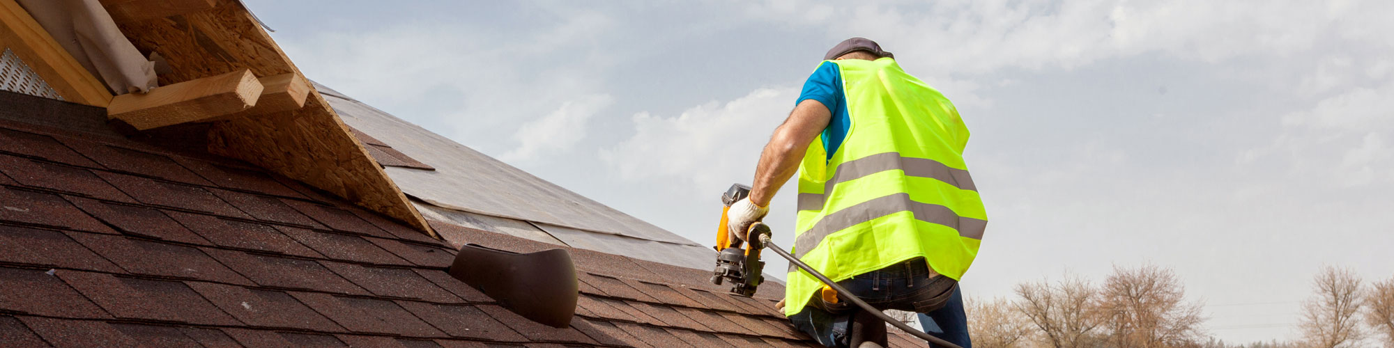 Construction Worker Putting The Asphalt Roofing (shingles) With Nail Gun On A Large Commercial Apartment Building Development